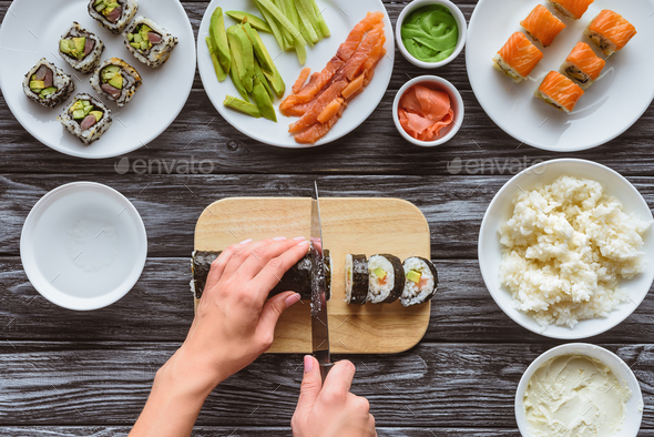 partial top view of person cutting delicious sushi roll with knife