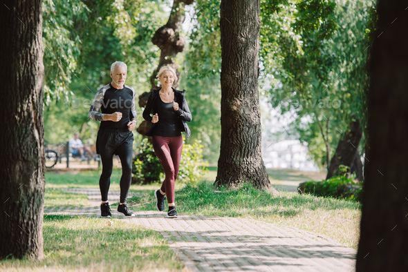 selective focus of smiling mature sportsman and sportswoman running together in park