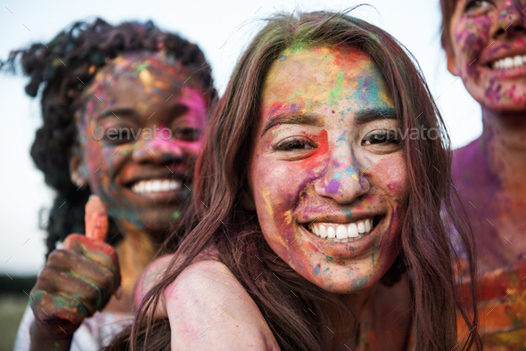 happy young multiethnic women with colorful paint on clothes and bodies having fun together at holi