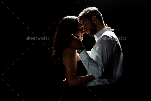 side view of bearded man touching hair of woman while standing isolated on  black Stock Photo by LightFieldStudios