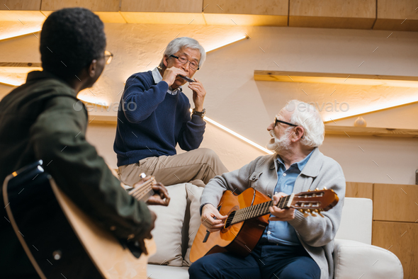 group of happy senior friends playing music with guitars and harmonica