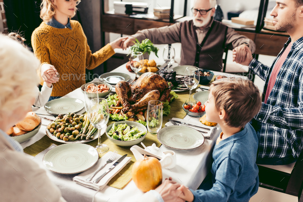 beautiful religious family holding hands and praying on thanksgiving before holiday dinner