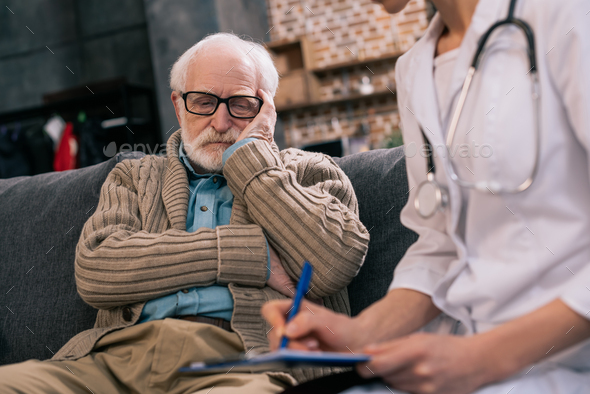 Sad senior man looking at doctor writing down medical complaints