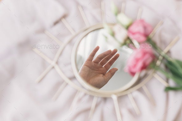 Hand reflected in mirror on background of soft fabric with eustoma flowers, aesthetic. Mental Health