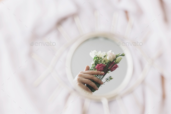 Hand holding flowers reflected in mirror on background of soft fabric. Womens day. Gentle image