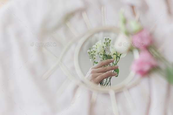 Hand holding manuka flowers reflected in mirror on background of soft fabric. Spring aesthetics