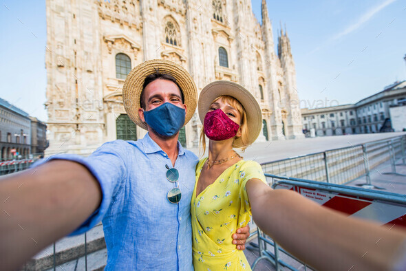 Friends wearing protective face mask taking a selfie in front of Duomo cathedral, Milan