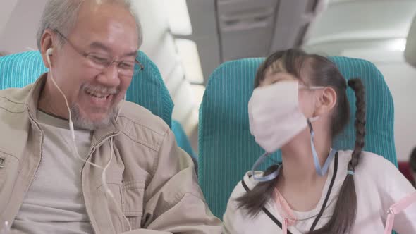 Happy Asian grandfather talking and laughing with granddaughter at seat in airplane