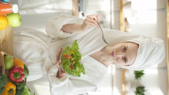 Woman in a White Coat and a Towel on Her Head Eats a Salad of Fresh Vegetables for Breakfast alt