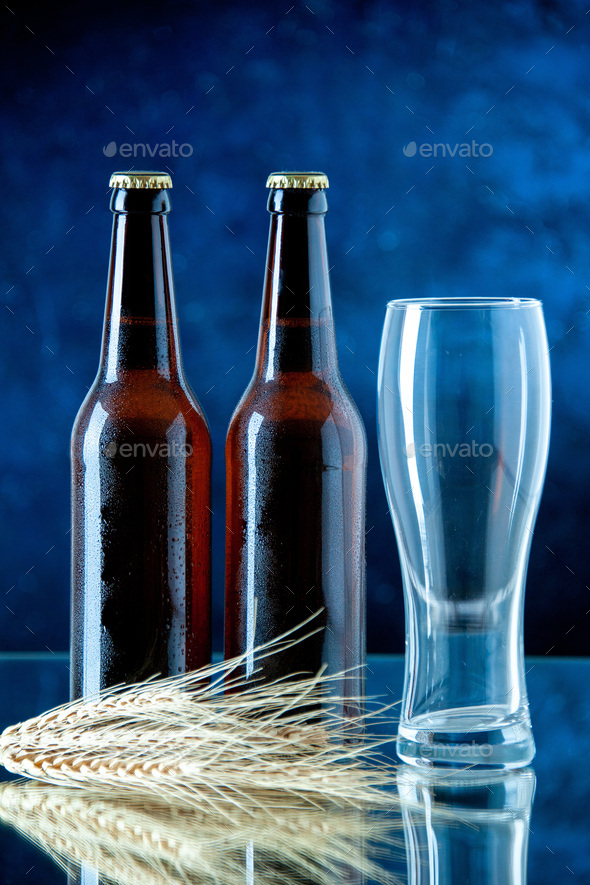 Vertical view of two full beer bottles and empty glass on blue background  Stock Photo by KamranAydinovStudio