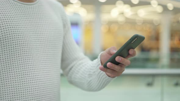 Pan Shot of Male Hand Scrolling a Phone on Blurred Yellow Background