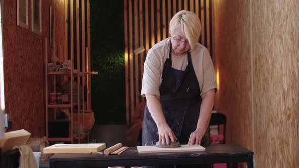 An Elderly Woman with Short Hair Throws a Piece of Clay on the Board alt