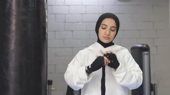 Arab Female Kickboxer in a White Hijab Ties a Black Elastic Armband Around Her Arm Before Boxing in