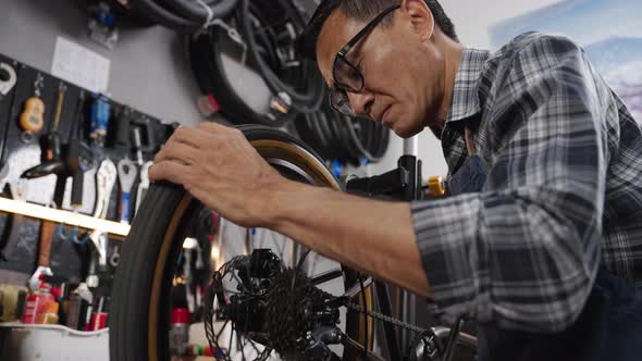 Asian senior man worker repairing and checking wheels and gears of bicycle
