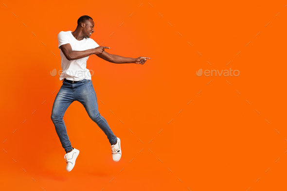 Millennial african american man pointing at copy space while jumping ...