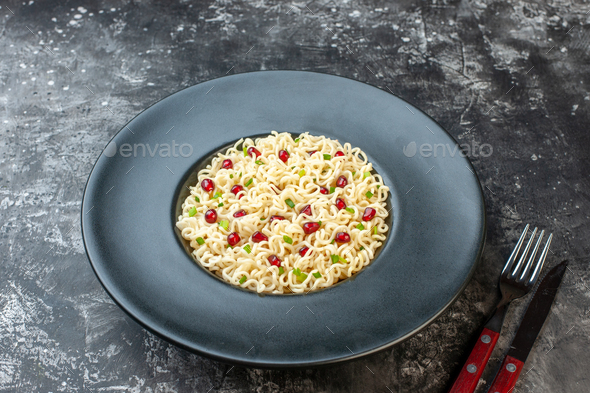 bottom view asian ramen noodles on black round plate fork and knife on dark table