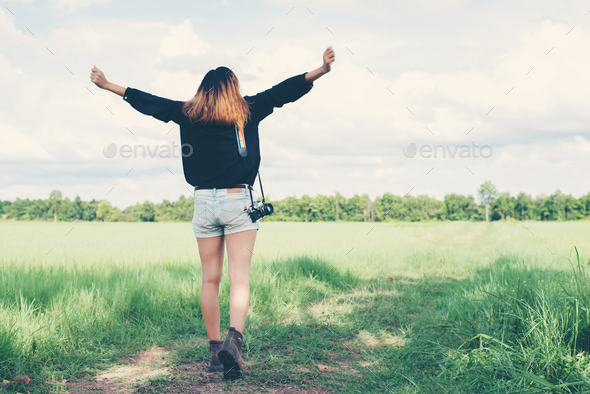 Back of young woman carrying retro camera in grass field enjoy to go take photo.