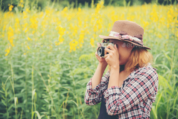 Happy woman in yellow flower field hloding with retro camera outdoors,enjoying nature.