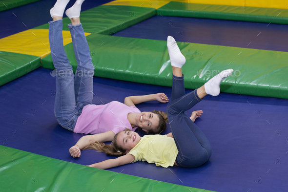 Cute teen girl and her happy mother lying on trampoline, lifting their legs up, having fun together