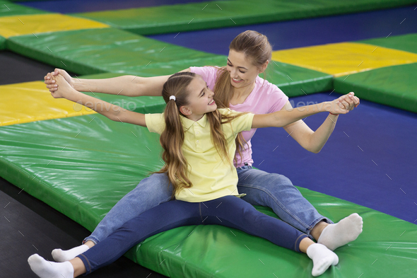 Adorable teenage girl with her joyful mom fooling around at trampoline park. Fun pastimes and