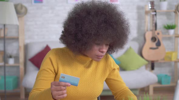 Beautiful African American Girl with an Afro Hairstyle with a Bank Card in Hand and a Laptop in the alt
