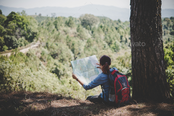 Young woman backpacker hiker reading map hiking trip looking away to find place to go.