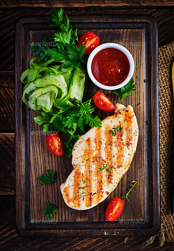 Grilled chicken breast with fresh vegetables on wooden cutting board