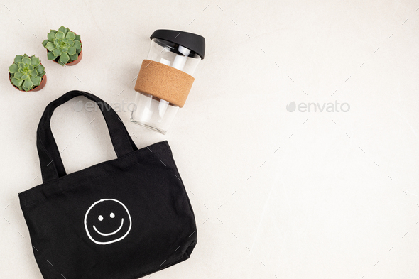 Black organic cotton cloth eco bag and reusable glass coffee cup on white background. Zero waste