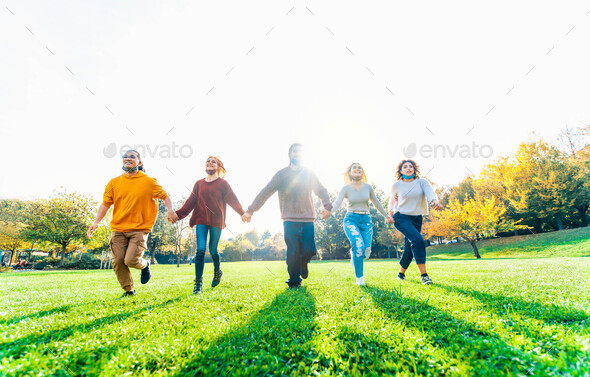 Multicultural people with open face mask running in the park after lockdown reopening - Stock Photo - Images