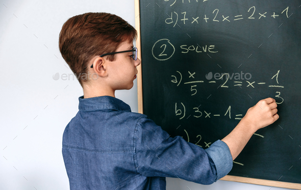 Boy solving math exercises on blackboard