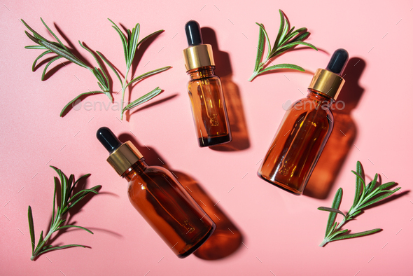 Dropper bottles with oil and rosemary leaves on pink table flat lay view. Herbal cosmetics concept