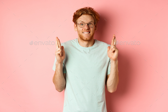 Worried redhead man waiting for results, expecting something with fingers crossed, biting finger and