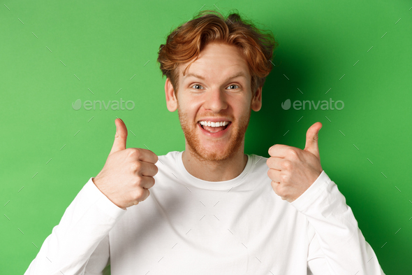 Emotions and fashion concept. Close up of cheerful redhead man showing thumbs-up and say yes