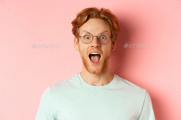Close up of surprised redhead man raising eyebrows and scream with joy, checking out cool promo
