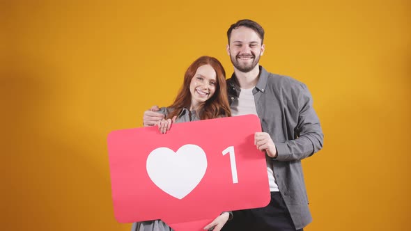 Man and a Woman Hold a Social Network Icon They Recommend Subscribing and Putting a Lot of Likes on alt