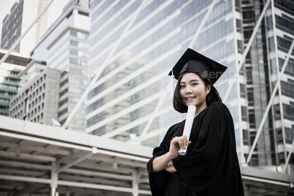 Young female graduates in square academic cap smiling happy holding diploma against building.