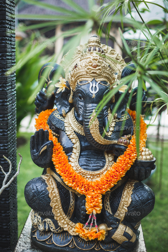 Ganesha statue in balinese garden with orange color flower necklace