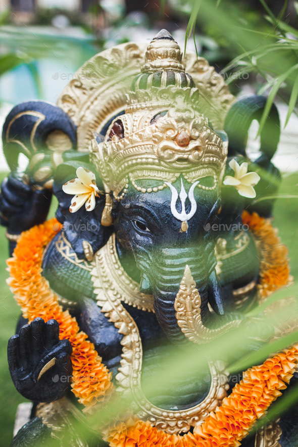 Ganesha statue in balinese garden with orange color flower necklace