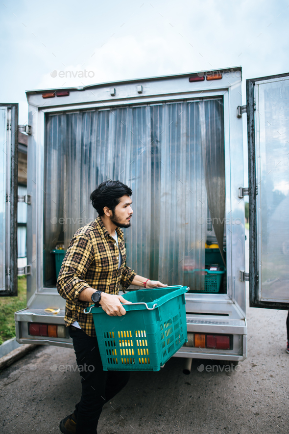 Portrait of a hipster farmer holding box of fruit lift up to the car to go market for sell.