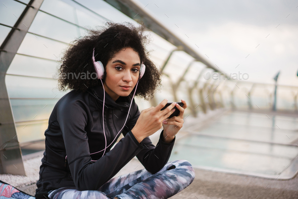 Focused athletic sportswoman in headphones using mobile phone