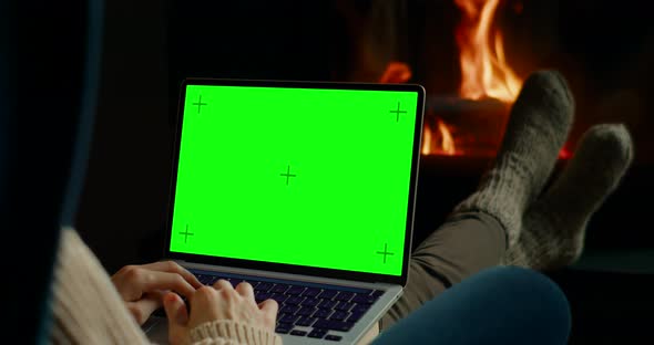 Woman Works on Laptop with Chromakey Green Screen at Fireplace in Home Office