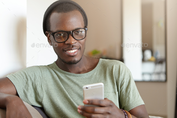 Indoor shot of male with dark skin wearing shades, cap and casual T-shirt resting at home at sofa ho - Stock Photo - Images