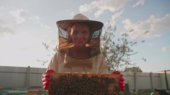 A Girl Beekeeper in a Protective Suit Carries a Frame with Honey From a Bee Hive