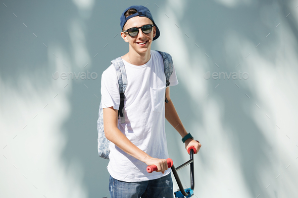 Healthy lifestyle concept. Cute teenage boy in sunglasses, carrying  backpack, looking and smiling at Stock Photo by wayhomestudioo