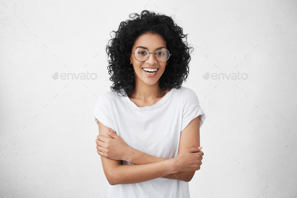 Pretty woman in white t-shirt and round eyeglasses feeling shy and a bit uncomfortable, smiling nerv