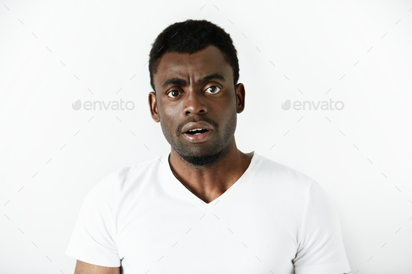 Headshot of puzzled black office worker in white polo shirt looking in shock and frustration at the