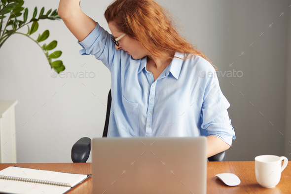 Portrait of a young woman wearing blue shirt disgusting with bad smell of her wet armpit while worki