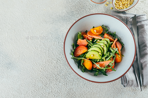 Healthy vegan salad bowl with salmon, tomato, avocado, arugula. Delicious balanced food concept.