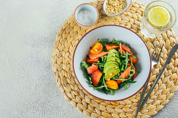 Healthy vegan salad bowl with salmon, tomato, avocado, arugula. Delicious balanced food concept.