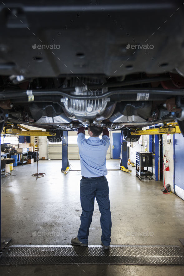 Mechanic in a repair shop works on the underside of a car up on a lift